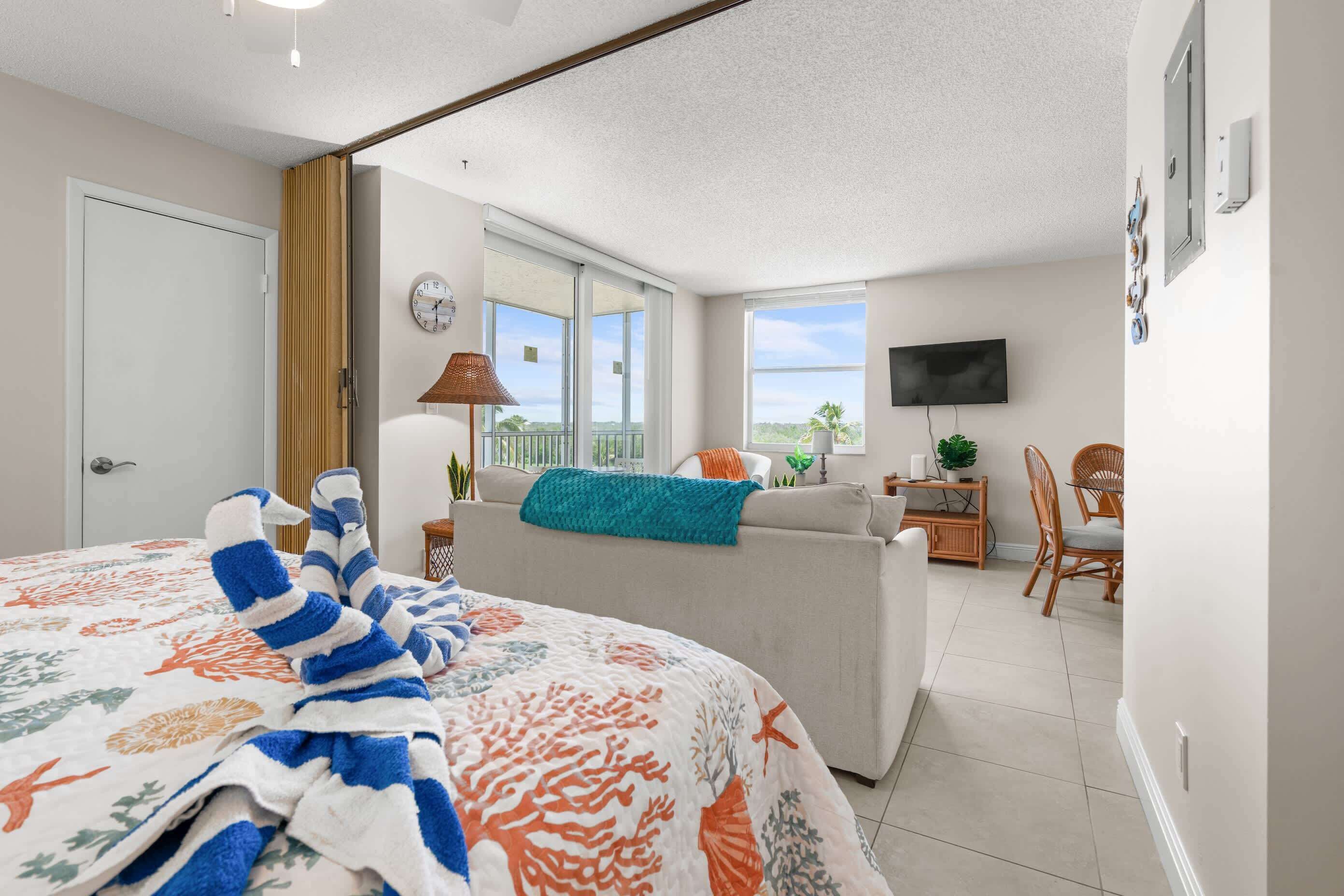 A bedroom with a bed, a sofa, a TV, a balcony, and a dining area.