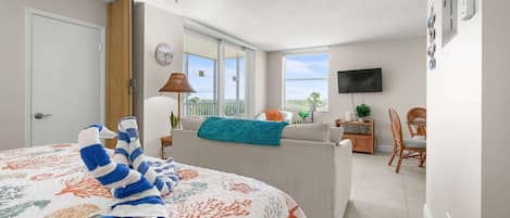 A bedroom with a bed, a sofa, a TV, a balcony, and a dining area.