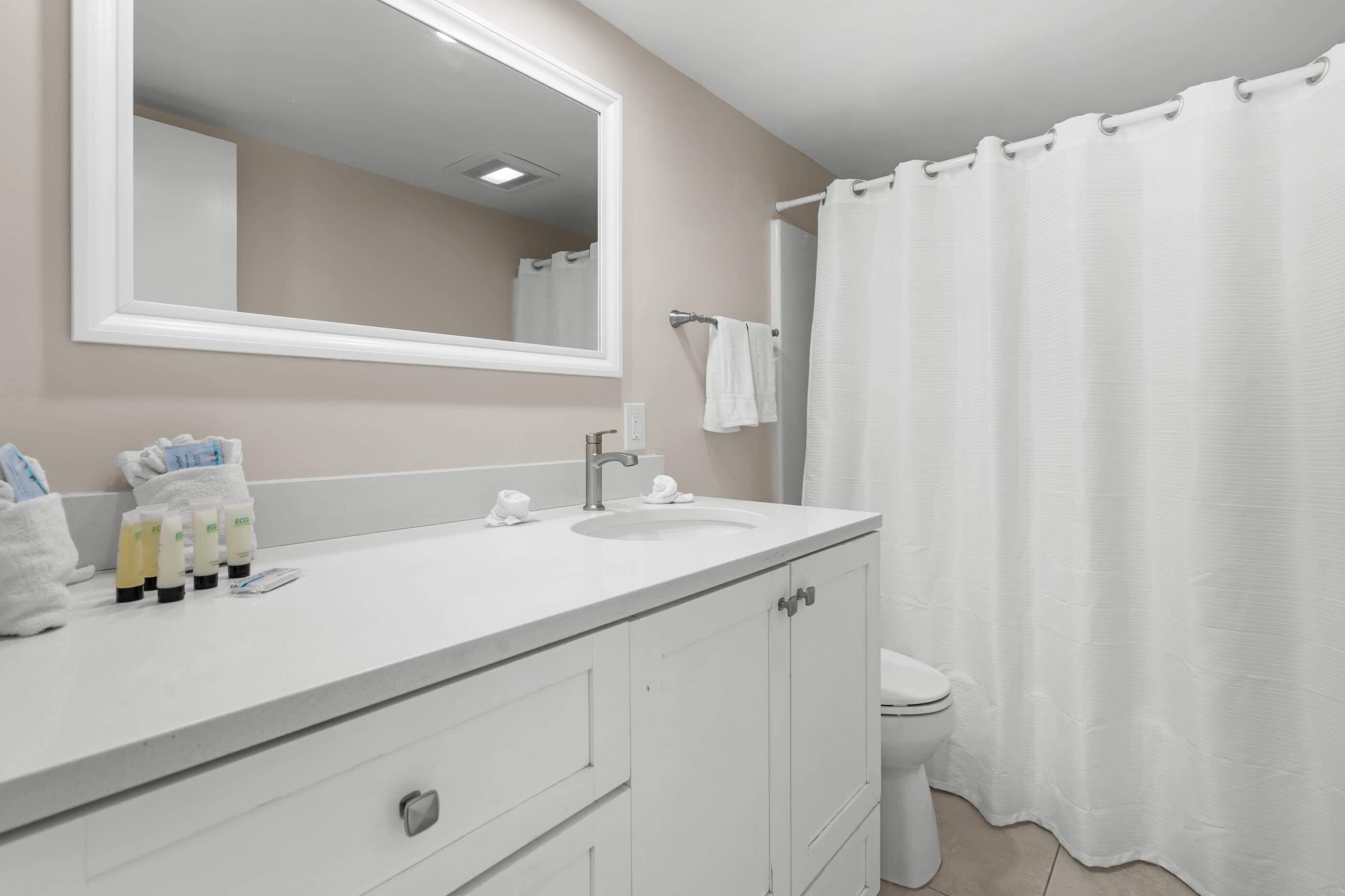 A bathroom with a white sink, mirror, and toilet. There are toiletries on the sink counter.