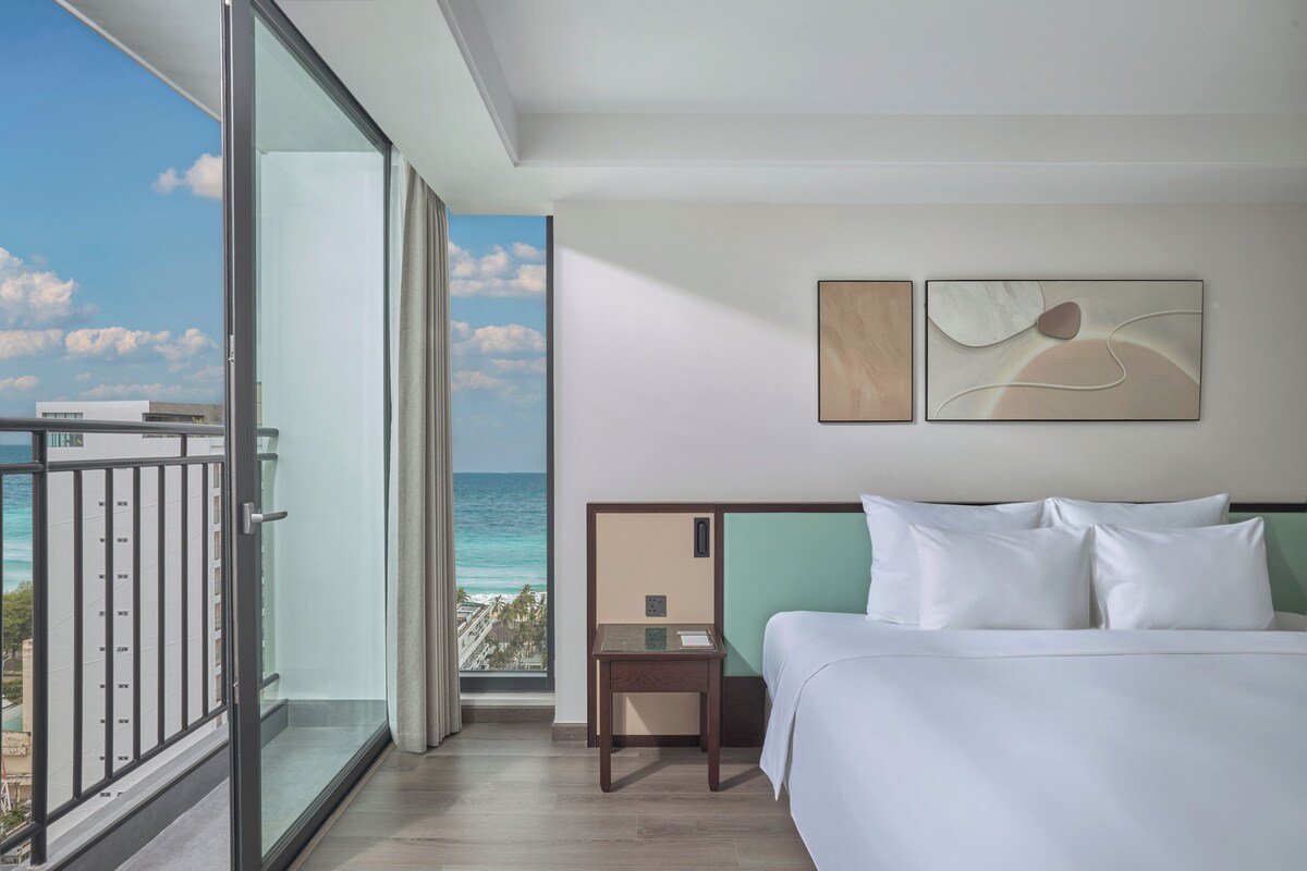 A hotel room with a bed, a nightstand, and a view of the ocean.