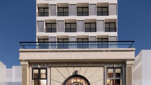 Une façade d’hôtel moderne, avec une entrée symétrique, de grandes fenêtres et une arche décorative centrale.