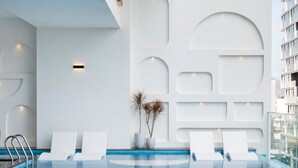 Une piscine intérieure moderne, avec des murs blancs et des motifs géométriques, des chaises longues et une eau d’un bleu cristallin.