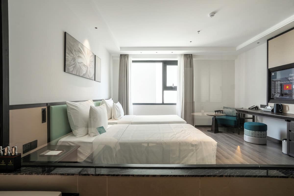 A hotel room with two beds, a desk, a chair, a television, and a window with curtains.
