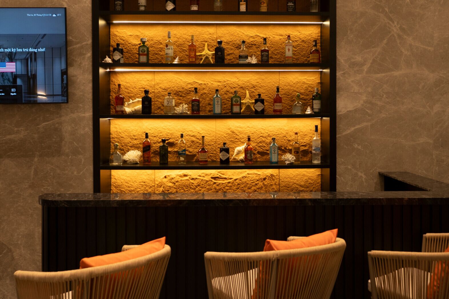 A bar area with multiple shelves of liquor bottles, wicker chairs, and a television screen displaying a message.