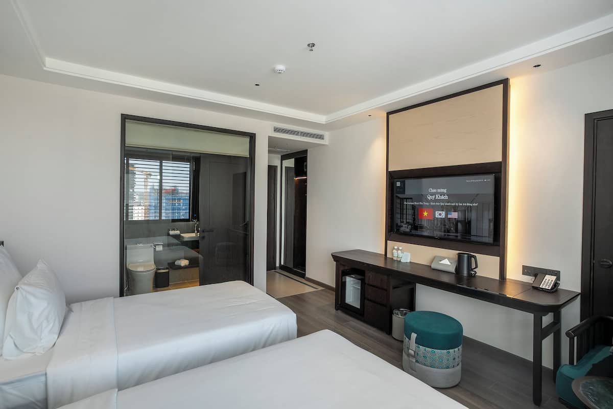 A hotel room with two beds, a desk with a computer, a mirror, and a TV.