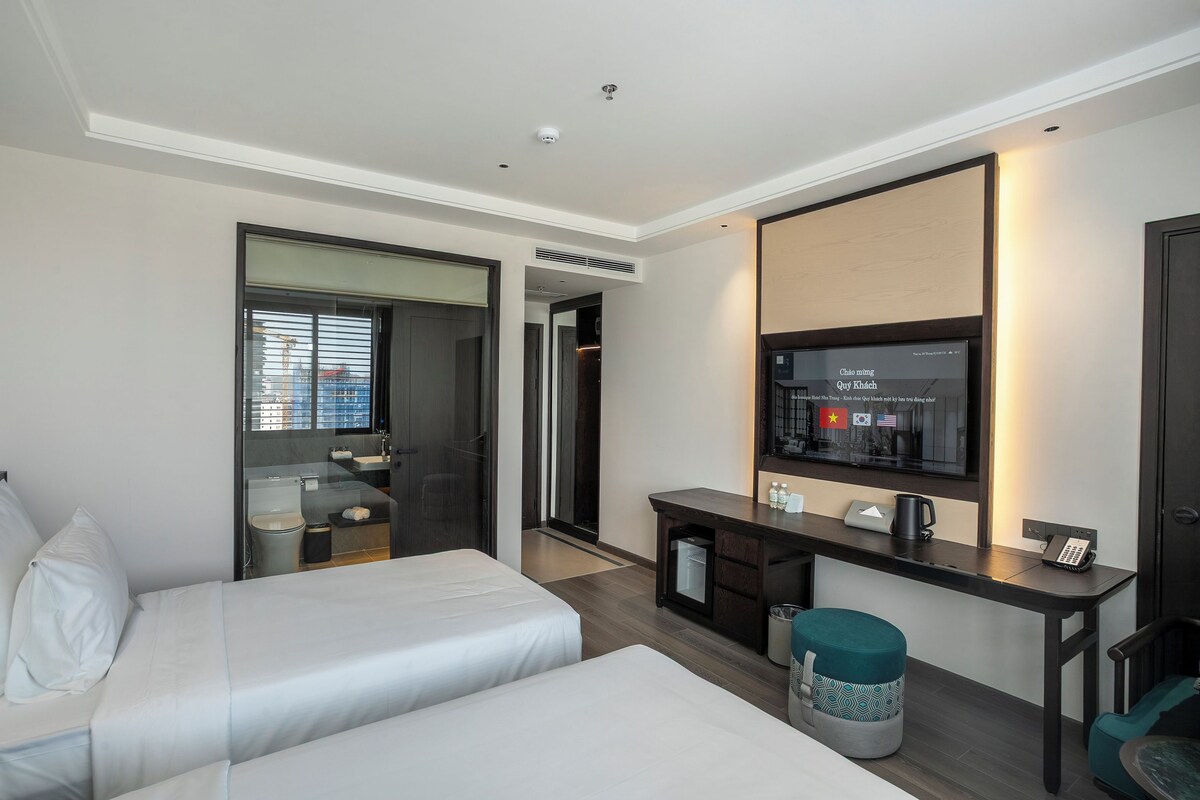 A hotel room with two beds, a desk with a computer, a TV, and a minibar.