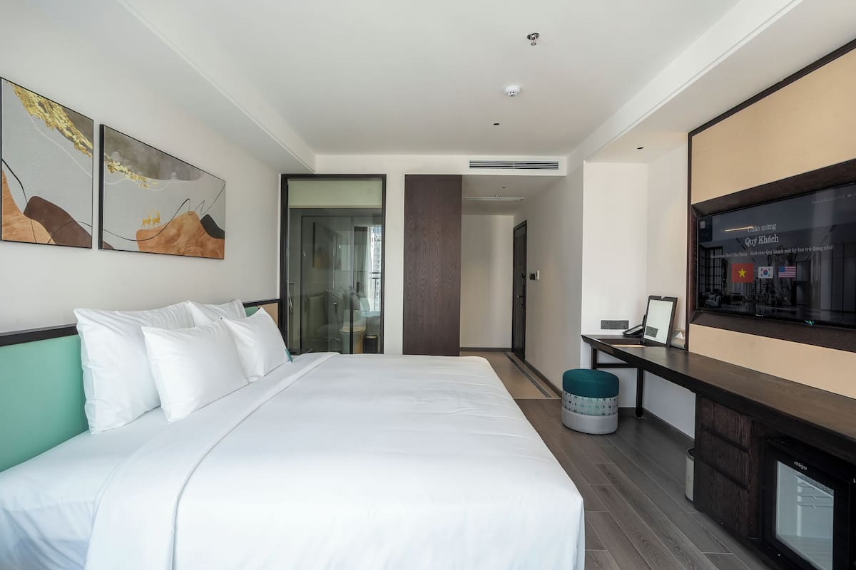 A modern hotel room with a large bed, a TV, and a desk area.