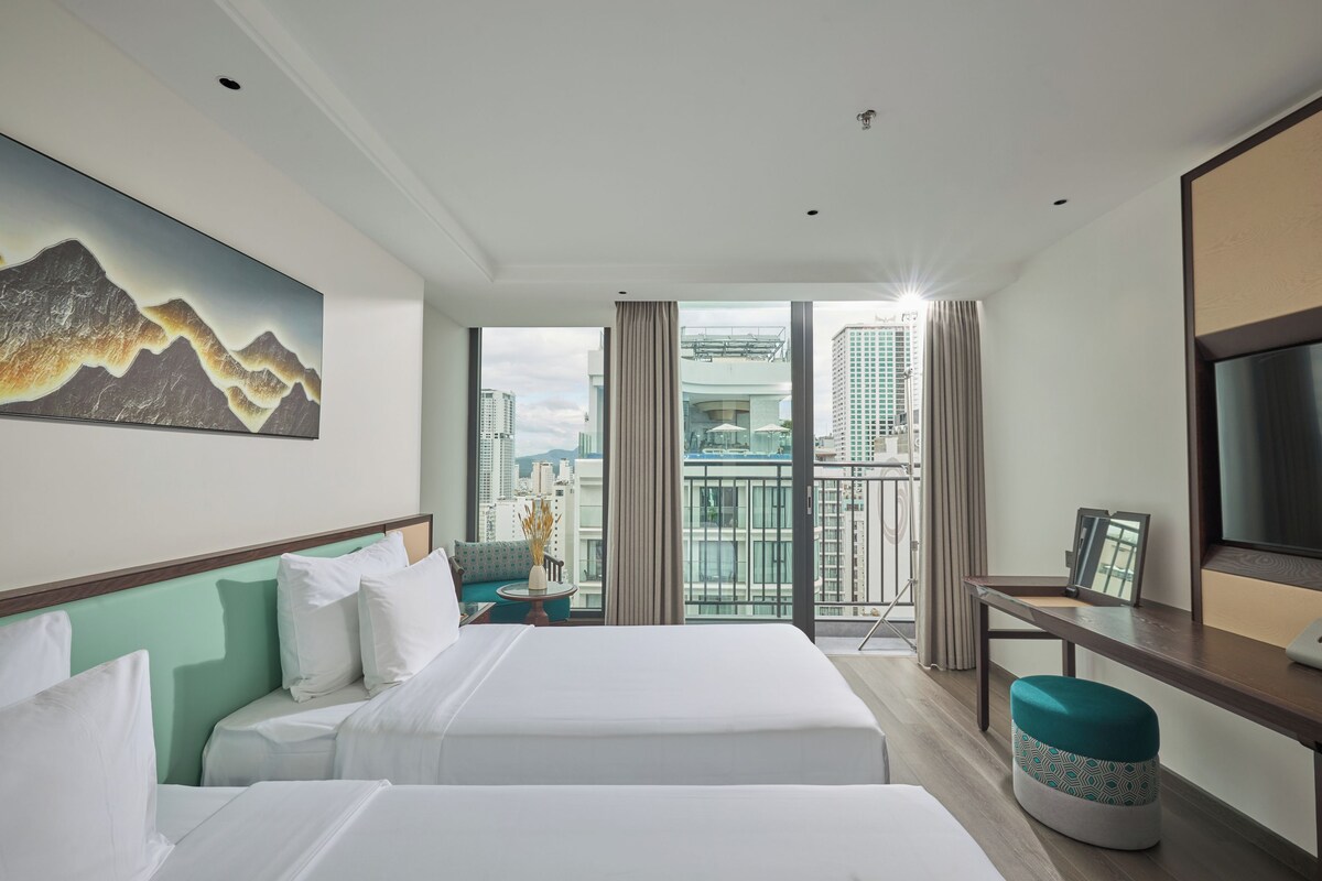 A hotel room with a bed, a desk, a TV, and a view of the cityscape.