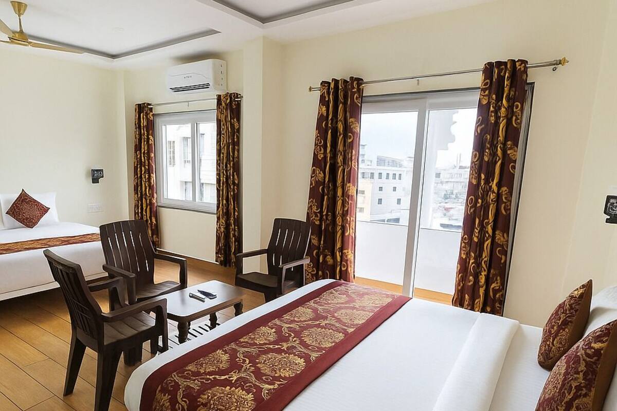 Ein Hotelzimmer mit einem großen Bett, zwei Sesseln, einem kleinen Tisch und einem Sofa. Es gibt ein Fenster mit Vorhängen, eine Klimaanlage und einen Deckenventilator.