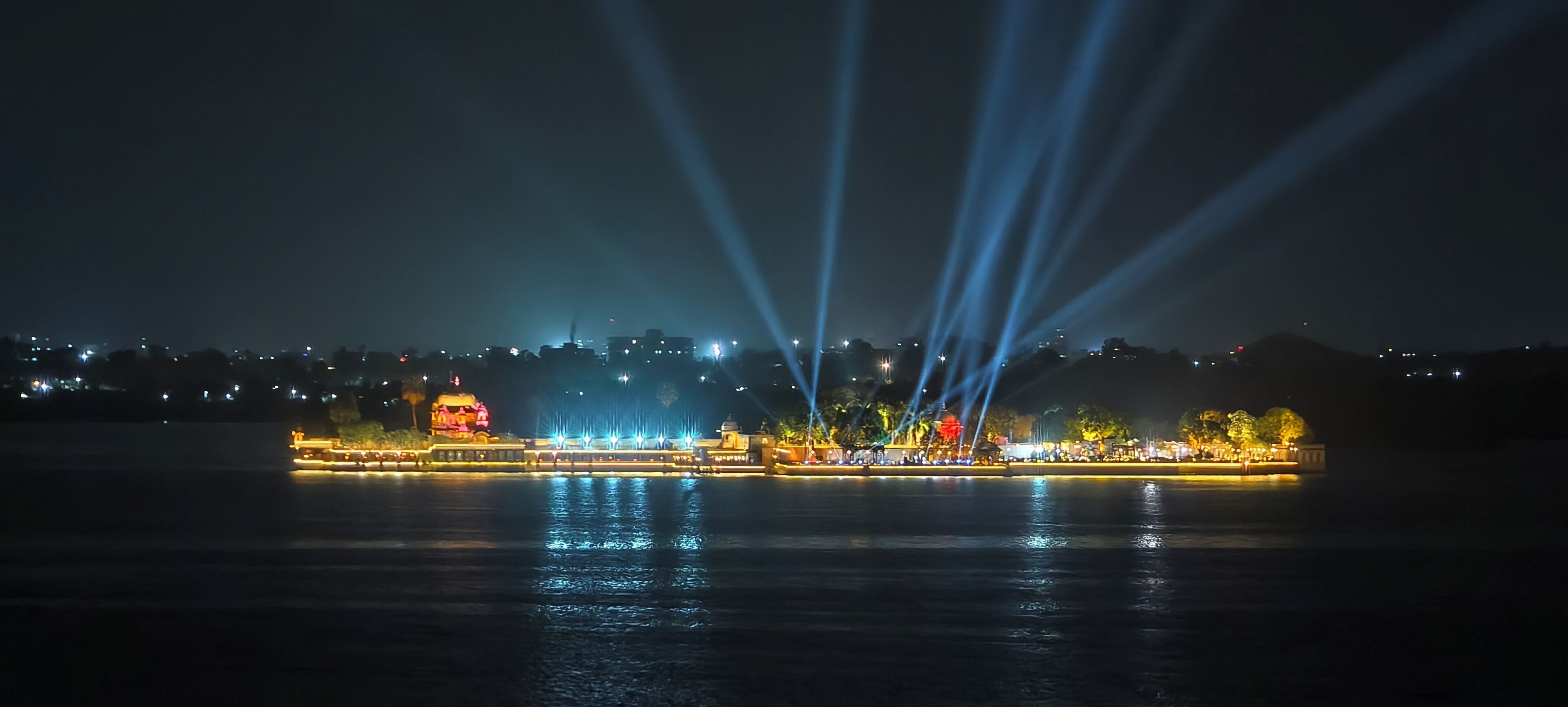 A nighttime view of a riverside area with illuminated buildings and a boat docked at the riverbank.