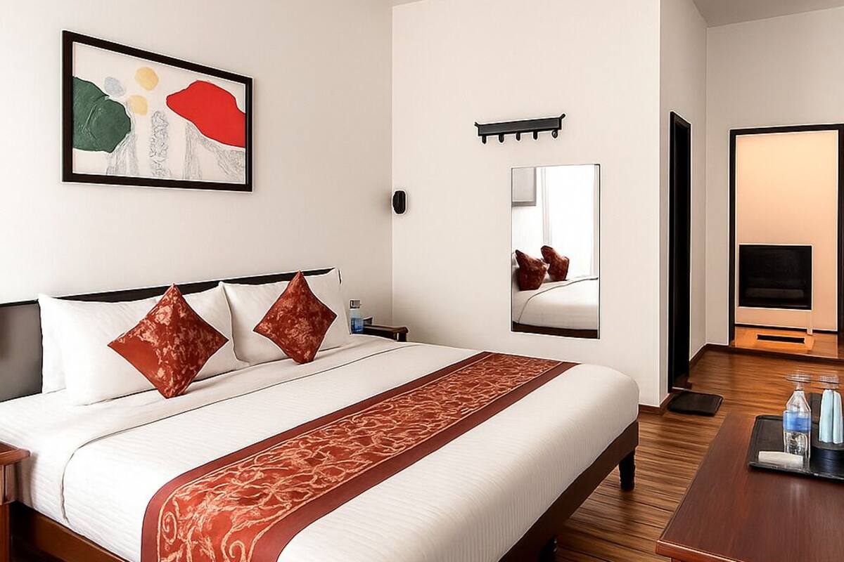 Ein Hotelzimmer mit einem großen Bett, Holzboden, einem Schreibtisch mit Stuhl, einem Fernseher und einem gerahmten abstrakten Gemälde an der Wand.