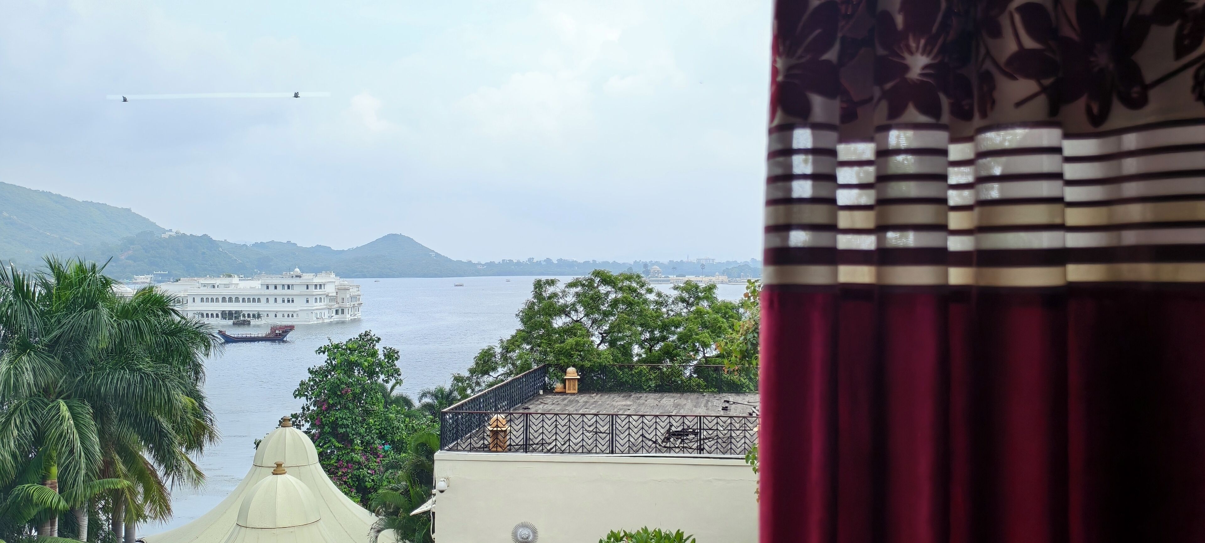 A view of a river with boats, a hill in the background, and a building with a white dome and a balcony.