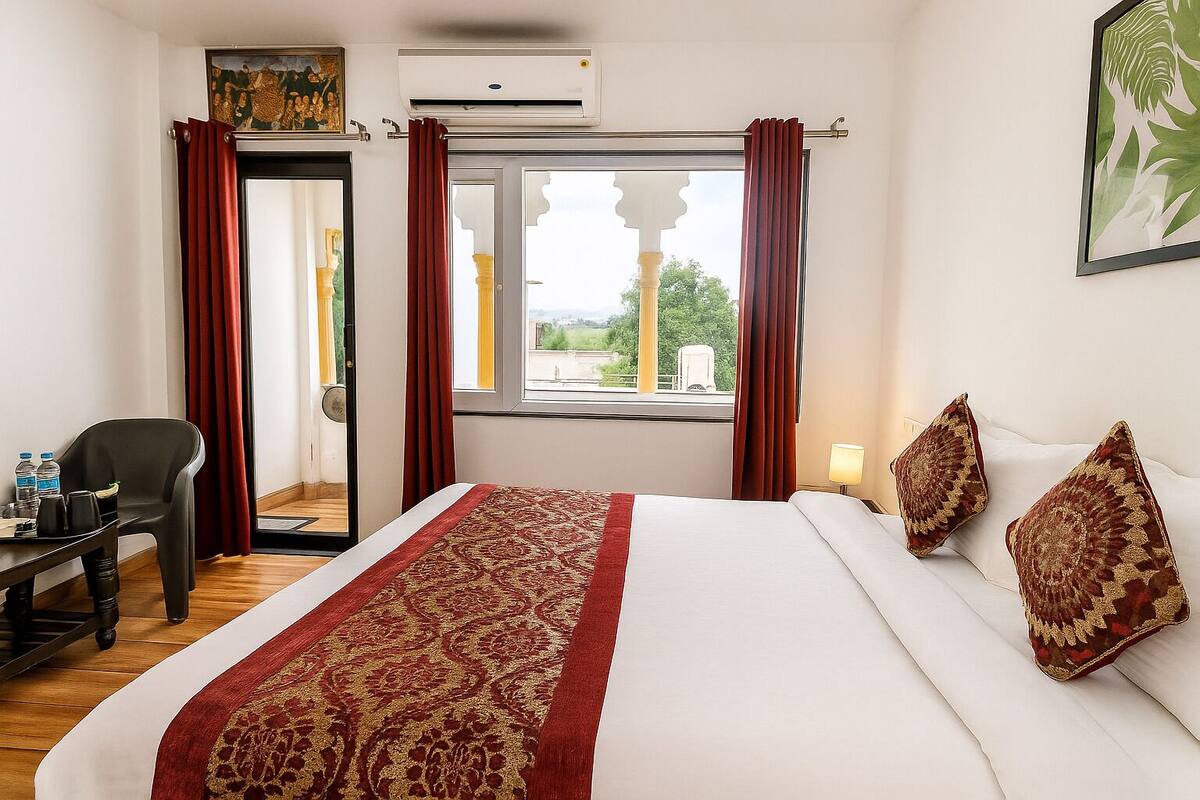 Ein Hotelzimmer mit Bett, Schreibtisch mit Stuhl, einem Fenster mit Vorhängen und einem Bild an der Wand.