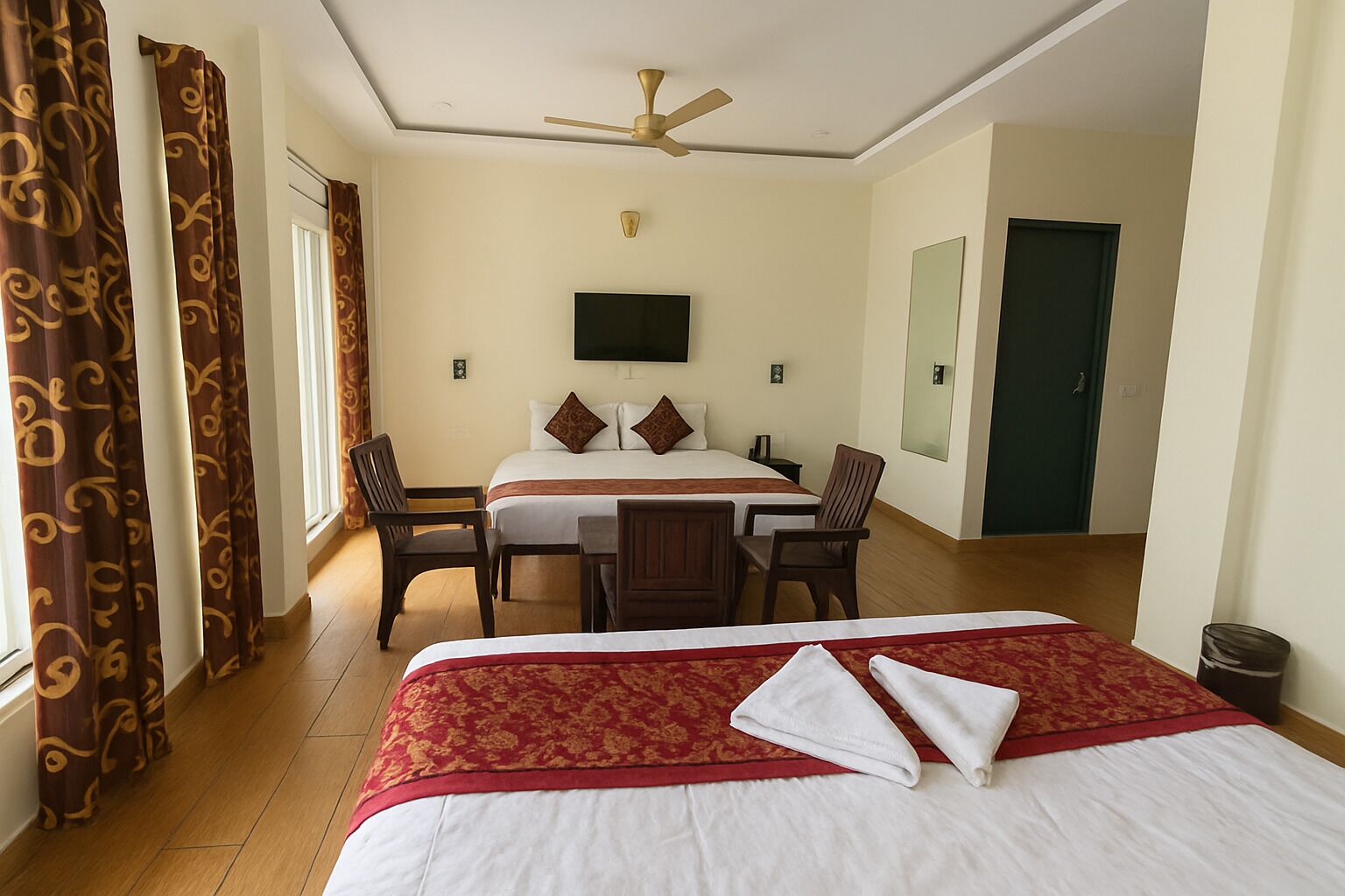 A hotel room with a large bed, a desk with two chairs, a ceiling fan, and a TV on the wall.