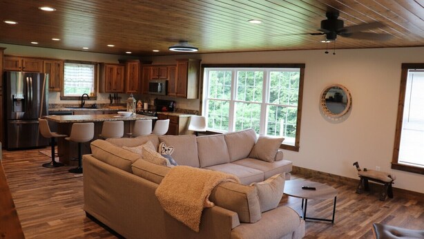 A spacious living room with a large beige sectional sofa, a wooden floor, and a kitchen area with wooden cabinets and a stainless steel refrigerator. - Mammoth Cave Cabin Rentals 12 (Mammoth Cave)