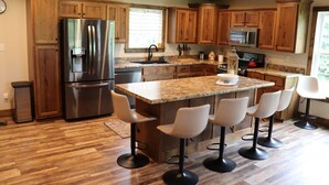 A modern kitchen with wooden cabinets, a stainless steel refrigerator, a granite countertop, and bar stools. - Mammoth Cave Cabin Rentals 12 (Mammoth Cave)