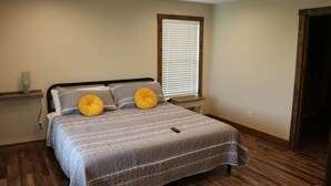 A bedroom with a bed, wooden flooring, a window with blinds, and a bedside table with a lamp. - Mammoth Cave Cabin Rentals 12 (Mammoth Cave)