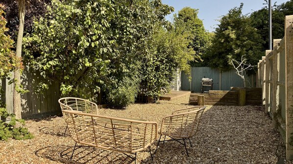 A patio area with wicker chairs, a barbecue grill, and a wooden deck. - Oyster Stay House By My Getaways (Whitstable)