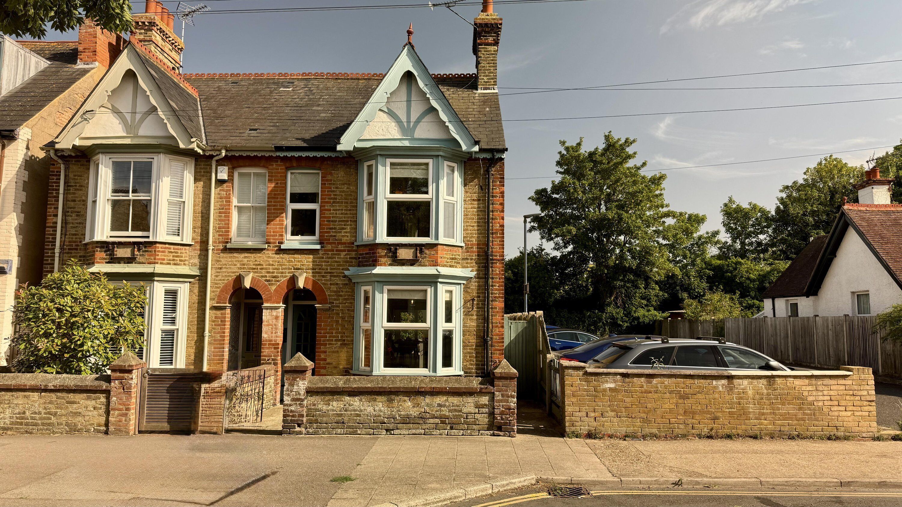 A two-story Victorian-style house with a brick facade, multiple bay windows, and a prominent gabled roof.