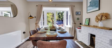 A dining area with a wooden table set for four, a fireplace, and a view of the outdoors.
