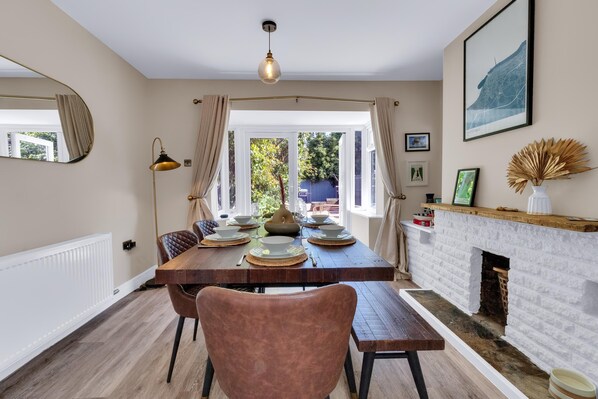 A dining area with a wooden table set for four, a fireplace, and a view of the outdoors. - Oyster Stay House By My Getaways (Whitstable)