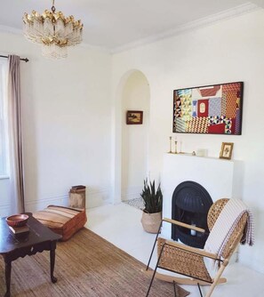 Un salon avec une cheminée, un lustre, un tableau et une plante en pot.