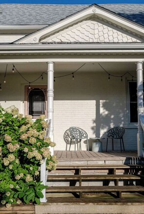A covered porch with wooden steps, two chairs, and a potted plant.