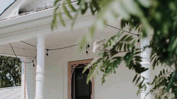 A white porch with a wooden staircase, a door, and a wicker chair.