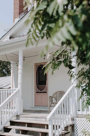 Une véranda blanche avec un escalier en bois, une porte et une chaise en osier.