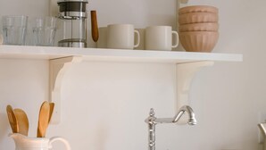 A kitchen with a wooden countertop, white cabinets, a sink, and a coffee maker.