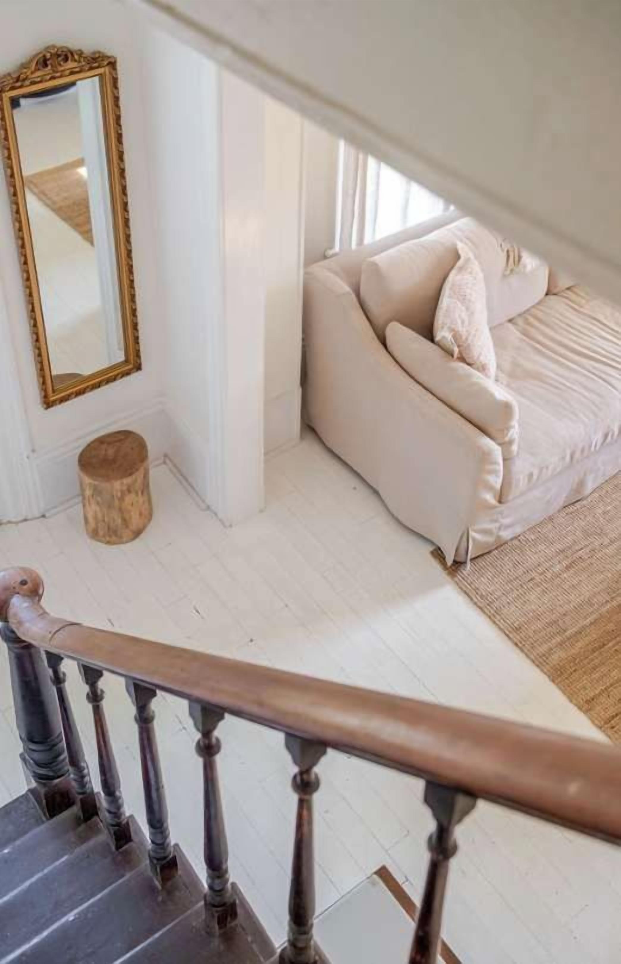 Un escalier menant à une chambre à coucher où se trouve un lit blanc et un grand miroir.