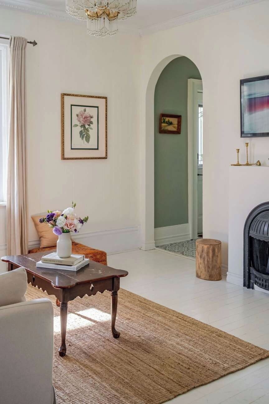 A living room with a fireplace, a coffee table with books, a vase of flowers, and framed artwork on the wall.