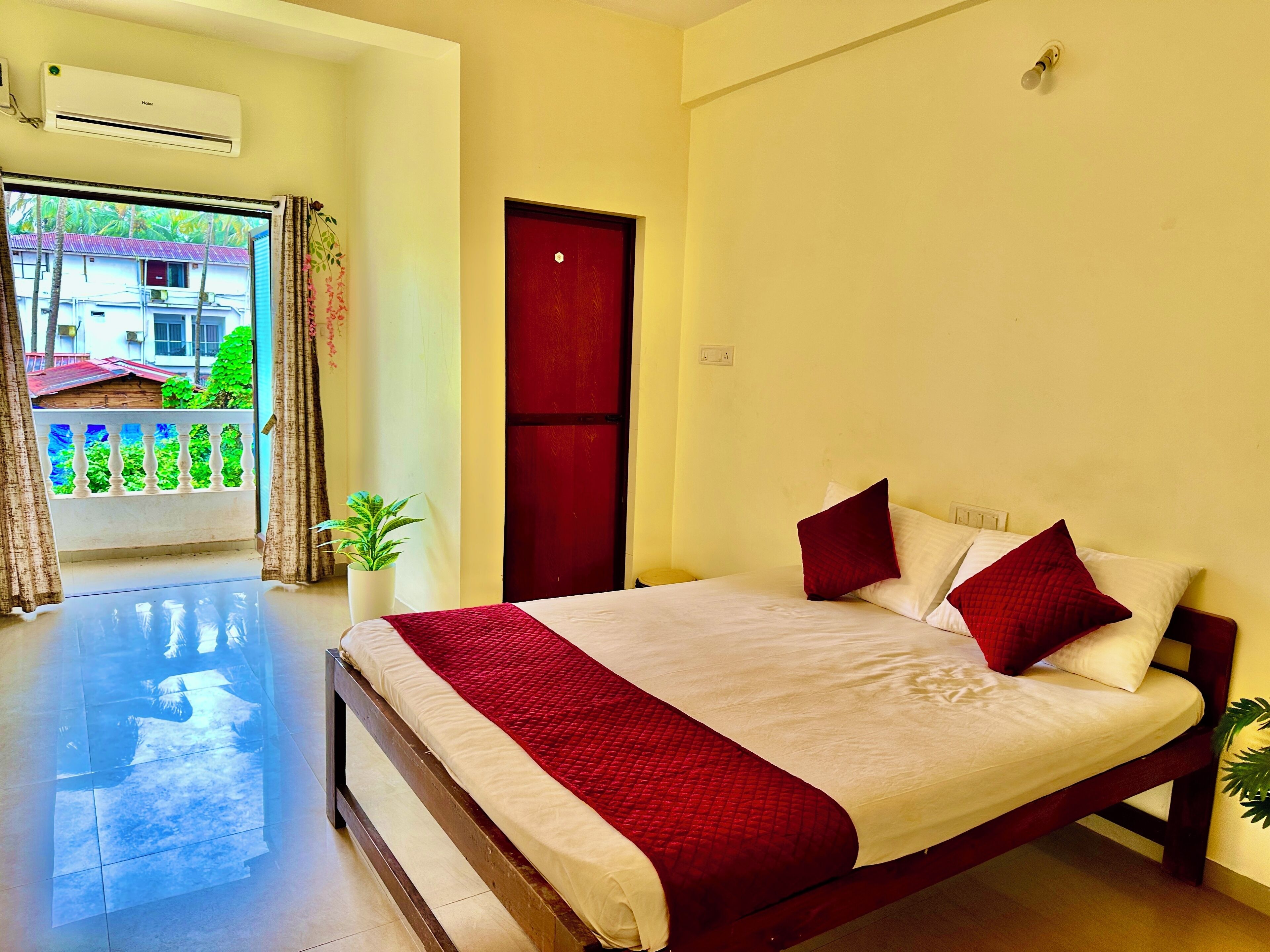 Une chambre d’hôtel avec un lit, une porte rouge, un balcon avec une balustrade et une plante en pot.