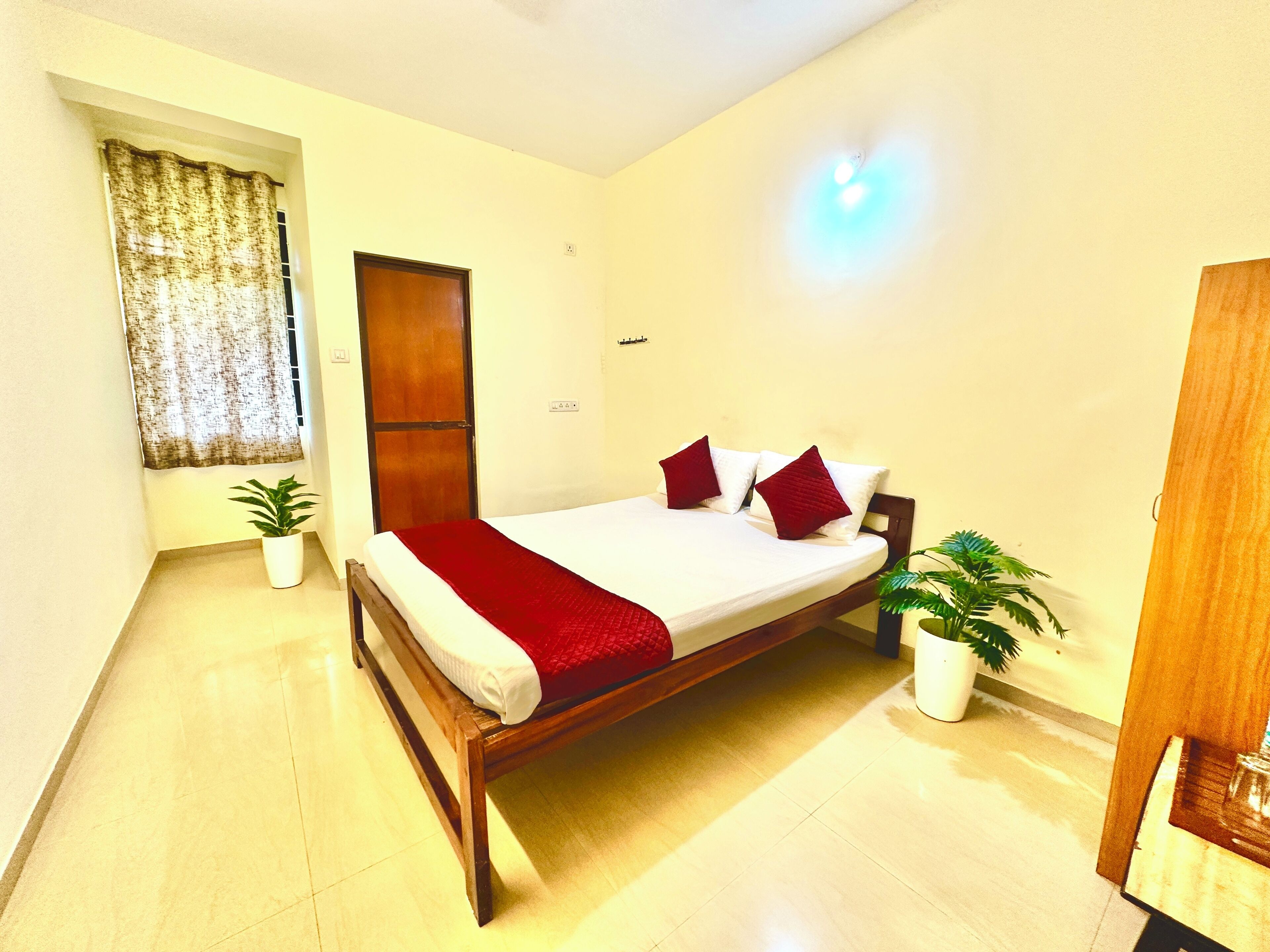 A bedroom with a wooden bed, a red blanket, and two potted plants.