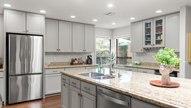 Una cocina moderna con gabinetes blancos, electrodomésticos de acero inoxidable, encimeras de granito y una isla central con fregadero.