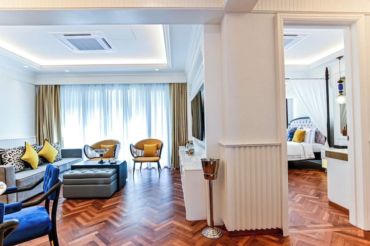 Ett modernt hotellrum med trägolv, en soffa, ett matbord och ett avskilt sovområde med en säng och ett nattduksbord.