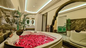 Un baño lujoso con una bañera grande llena de pétalos de rosa, paredes de mármol y decoración moderna.