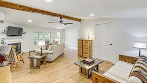 A spacious living room with hardwood floors, a fireplace, a sofa, a coffee table, and a television. - Serene Cabin w/ Pond & Creek on South Saluda River (Cleveland)
