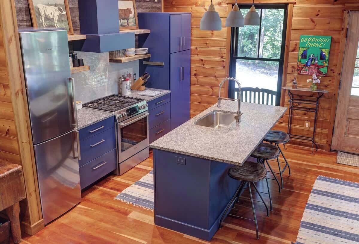 A modern kitchen with blue cabinets, a stainless steel refrigerator, a gas stove, and a bar area with stools.