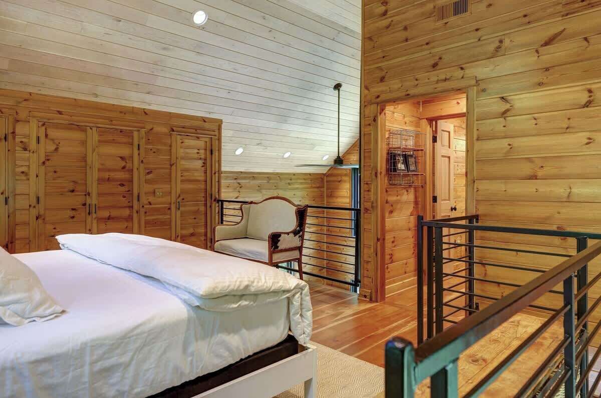 Une chambre aménagée dans une cabane en bois, avec un lit, une chaise, une petite table et un escalier.