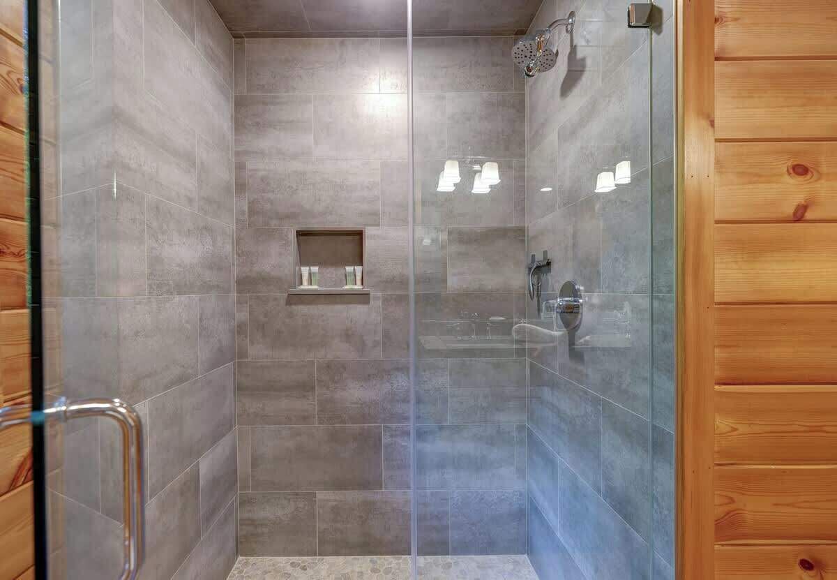Una ducha con paredes de vidrio, una puerta de madera y un estante con artículos de aseo.