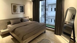 Un dormitorio moderno con una cama grande, un ventilador de techo, una mesita de noche, un cuadro enmarcado, un ventanal con cortinas y un espejo.