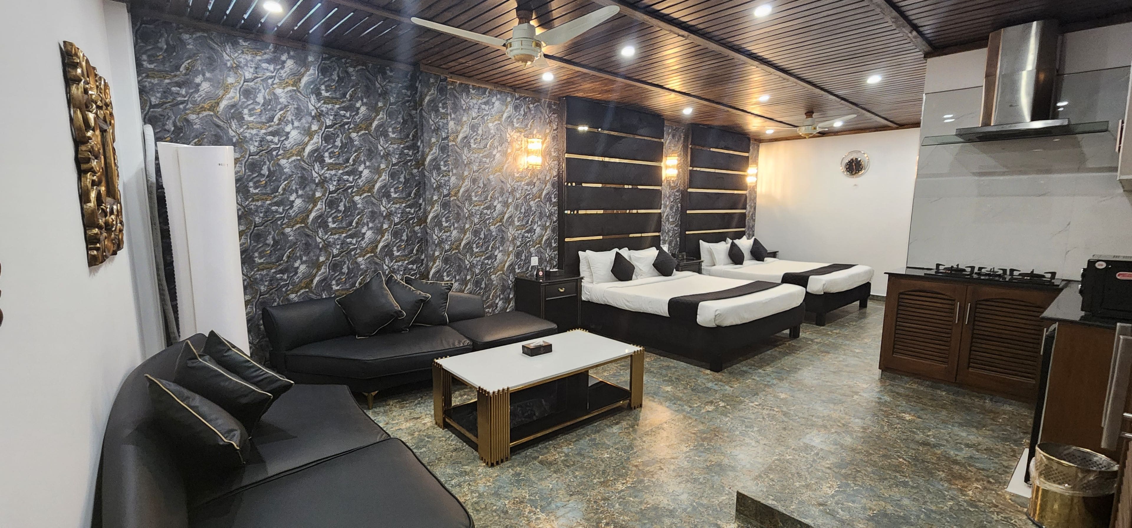 A modern hotel room with a marble wall, a sofa, a bed, a small table, and a kitchenette.