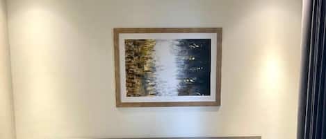 A modern hotel room with a large bed, a headboard, and a framed artwork on the wall.