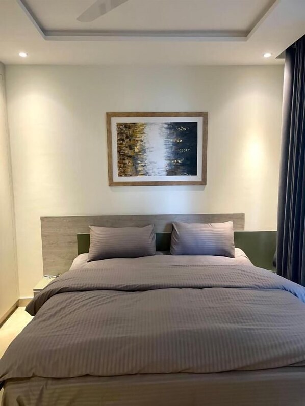 A modern hotel room with a large bed, a headboard, and a framed artwork on the wall. - Luxury Apartments by LVH (Lahore)
