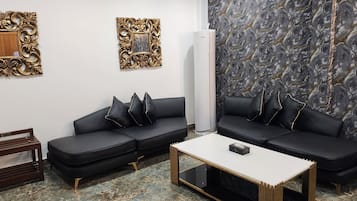 A modern living room with a black leather sofa, a white coffee table, and a marble-patterned wall.