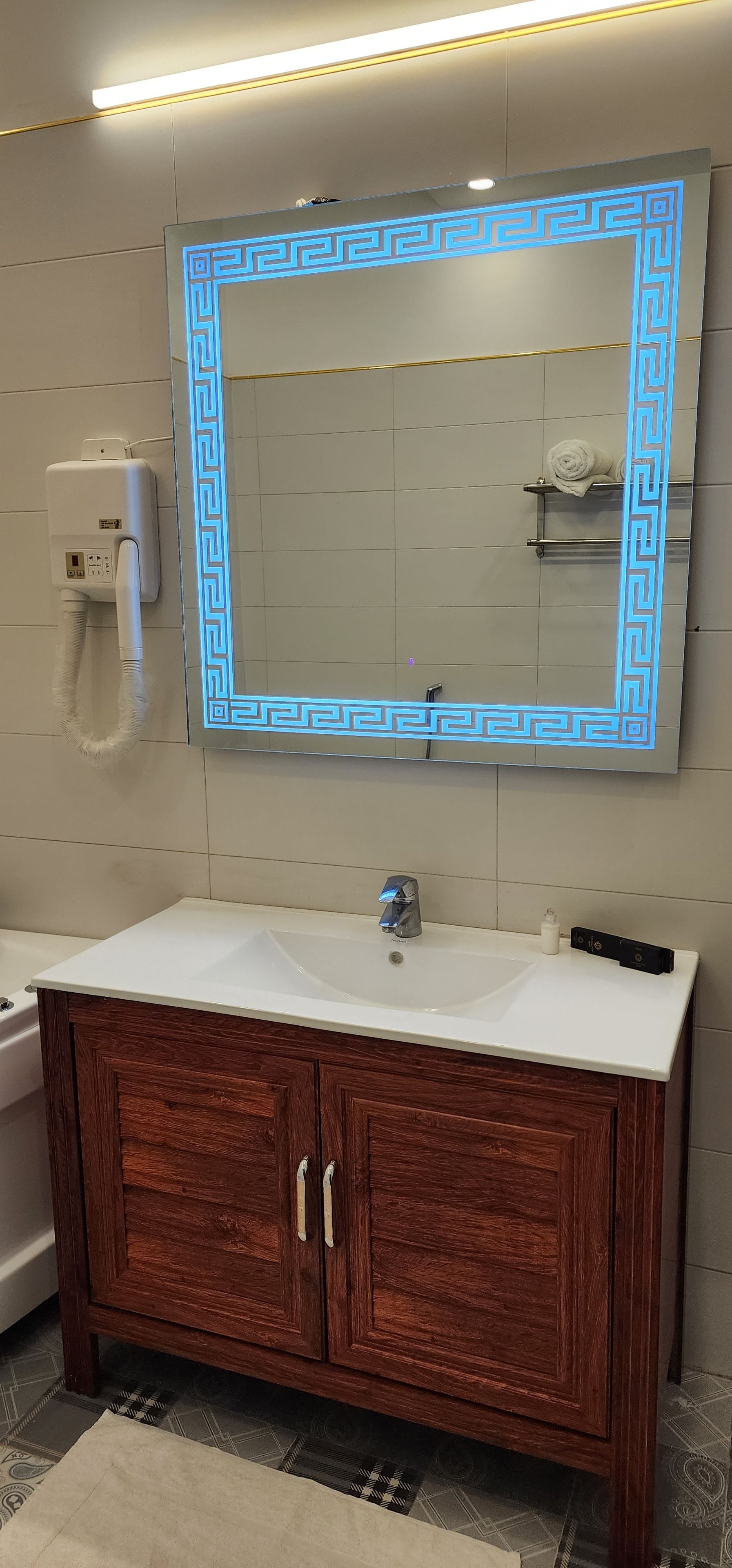 A bathroom with a large mirror, a sink, a towel rack, and a hairdryer.