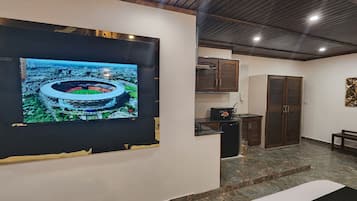 A modern interior with a large flat-screen TV mounted on a wall, a kitchen area with cabinets and a refrigerator, and a seating area with a bench.