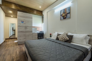 A modern bedroom with a large bed, a wooden wardrobe, a desk with a chair, and a painting on the wall. - Stay Studio Hotel & Residences (Gurugram)