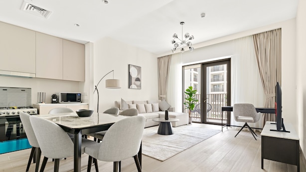 A modern kitchen with a stove, microwave, and dining area with chairs and a table. - Lotus at Creek Beach 1 - 407 2BD (Dubai)